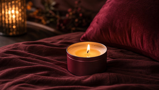 Low-temp massage candle glowing on dark linen in a warm bedroom