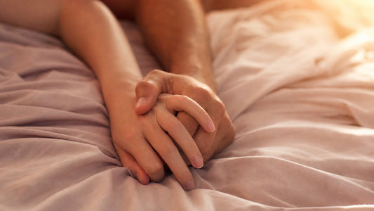 Two hands intertwined on soft sheets showing trust and connection during anal foreplay