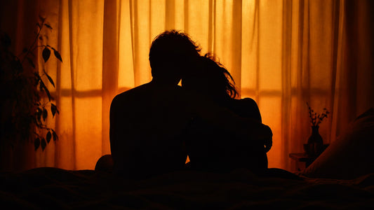 Silhouette of a couple embracing seated together backlit by warm amber light, cradle sex position