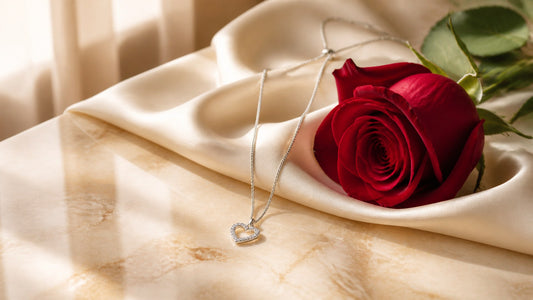 Silver slip chain day collar necklace with heart pendant on cream silk beside a red rose