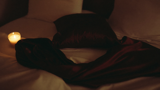 Soft black silk blindfold on white linen sheets with warm candle glow, intimate bedroom atmosphere