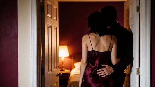 Couple silhouette in softly lit bedroom doorway, burgundy silk slip, intimate stolen moment