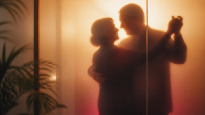 Silhouette of a mature couple slow dancing behind frosted glass in warm golden light, comfortable sex positions for older couples