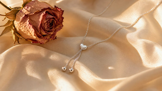 Silver heart slip chain necklace on cream silk with a dried rose