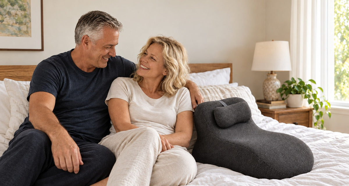Smiling couple sitting close together on a bed next to the WildNightX Pillow